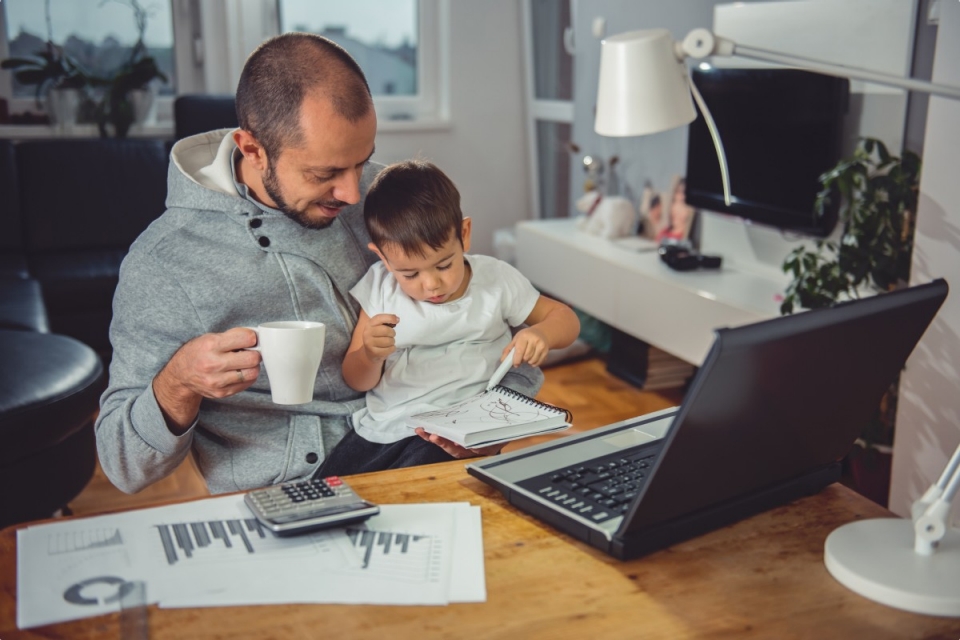 Man working at home with child on his lap and holding coffee cup