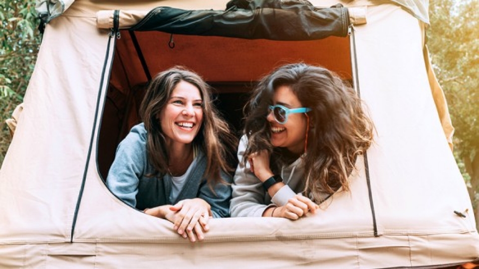 Two dark haired women laughing in a tent 